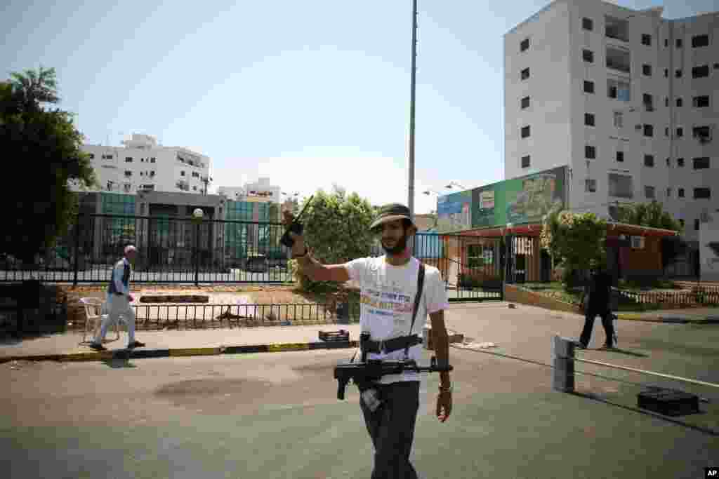 A local militiaman gestures to a car to stop at a checkpoint in Tripoli. The militia reported recent sniper fire from the white apartment block behind them (right), August 27, 2011 (VOA - J. Weeks)
