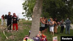 People stand at a memorial at the fatal crime scene where a man driving a pickup truck jumped the curb and ran over a Muslim family in what police say was a deliberately targeted anti-Islamic hate crime, in London, Ontario, Canada on June 7, 2021.