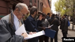 Un hombre revisa su hoja de vida, mientras espera en línea junto a otras personas que buscan trabajo en Nueva York.