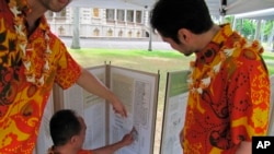 FILE - Dancers from the hula group Na Lei Hulu I Ka Wekiu look at a display of Hawaiian language newspapers on the Iolani Palace grounds in Honolulu, July 21, 2012.