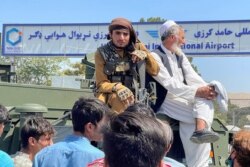 Seorang anggota pasukan Taliban (kiri) duduk di atas kendaraan lapis baja di luar Bandara Internasional Hamid Karzai di Kabul, Afghanistan, 16 Agustus 2021. (REUTERS/Stringer)
