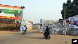 Members of the Party Loyalists drive their motocycles outside the entrance of a park in front of posters featuring Nigeria's opposition leader Mohammadu Buhari (R) and Nigeria's President Goodluck Jonathan and his Vice President Namadi Sambo (L) in Kad