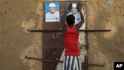 Young man glues campaign posters for Ibrahim Boubacar Keita on top of a pair posters for rival Dramane Dembele, Gao, Mali, July 25, 2013.