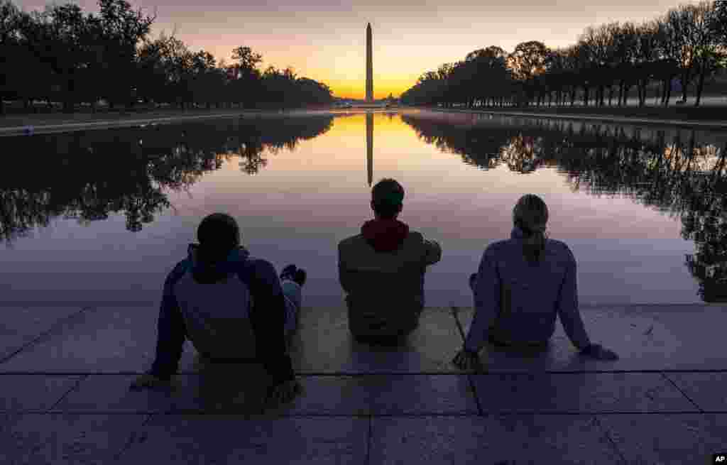A trio of friends watch the sunrise at the Reflecting Pool near the Lincoln Memorial in Washington, Thursday, Nov. 5, 2020, two days after Election Day. (AP Photo/J. Scott Applewhite)