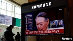 2024년 12월 윤석열 전 한국 대통령의 내란 혐의 선고 재판 관련 뉴스 보도를 방송하는 TV 화면 옆에 한 사람이 서 있다.