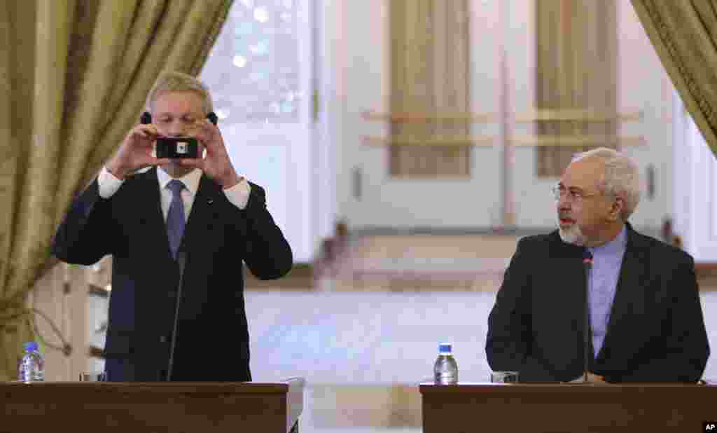 Swedish Foreign Minister Carl Bildt, left, takes a picture with his mobile phone as his Iranian counterpart Mohammad Javad Zarif watches him during their news briefing in Tehran, Iran.