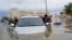 In this video grab from AFPTV, people push a stranded car along a flooded street in Dubai on April 16, 2024.