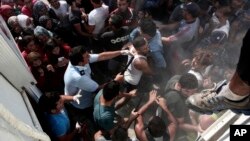 A policeman hits a migrant as police try to disperse hundreds of migrants during a registration procedure that was taking place at the stadium of Kos town, on the southeastern island of Kos, Greece, Aug. 11, 2015. 