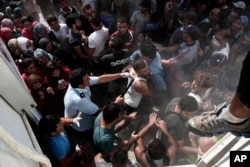 FILE - A policeman hits a migrant as police try to disperse hundreds of migrants during a registration procedure that was taking place at the stadium of Kos town, on the southeastern island of Kos, Greece, Aug. 11, 2015.