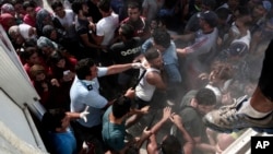 A policeman hits a migrant as police try to disperse hundreds of migrants during a registration procedure that was taking place at the stadium of Kos town, on the southeastern island of Kos, Greece, Aug. 11, 2015. 