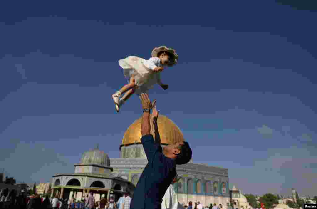 A Palestinian man throws his child in the air following morning prayers marking the first day of Eid al-Adha celebrations, on the compound known to Muslims as al-Haram al-Sharif and to Jews as Temple Mount in Jerusalem&#39;s Old City.