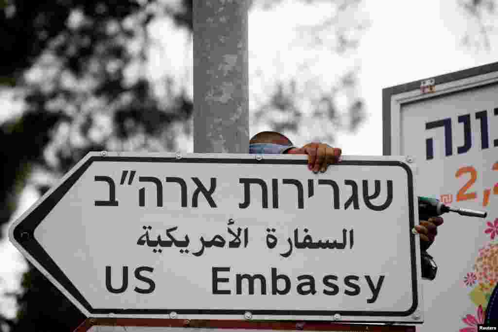 A worker hangs a road sign directing to the U.S. embassy, in the area of the U.S. consulate in Jerusalem.