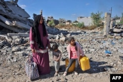 Seorang perempuan Palestina yang mengungsi berdiri bersama anak-anaknya di puing-puing bangunan hancur di jalan utama Salah al-Din, Kota Gaza di Beit Lahia, Jalur Gaza utara, 22 Oktober 2024. (Foto: AFP)