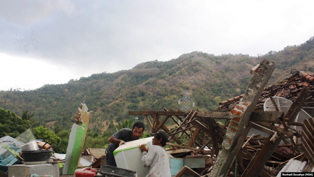 Dua warga Menggala, Lombok Utara, berusaha mengeluarkan mesin cuci dan reruntuhan rumah.