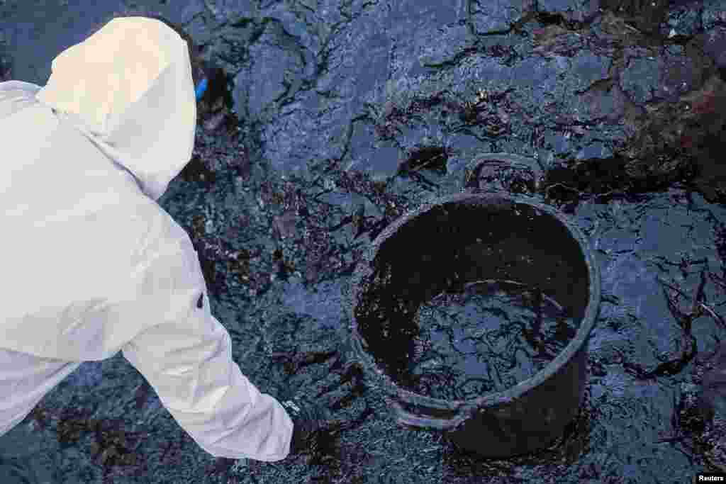 Một công nhân lau rửa đá bị dầu bao phủ trong một sự cố tràn dầu tại bãi biển Cabron, đảo Canary thuộc nhóm đảo Gran Canaria của Tây Ban Nha, ngày 16 tháng 7, 2014. Chưa rõ nguồn gốc của sự cố tràn dầu.