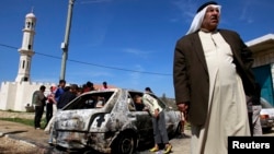 A Palestinian stands near a burnt car in the West Bank village of Kusra, near Nablus, February 21, 2013.