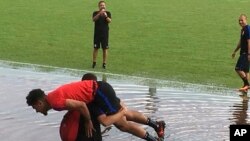 Pemain tim nasional AS, DeAndre Yedlin digendong pelatih Luis Ramirez melewati genangan air di sekitar lapangan tempat latihan, di Couva, Trinidad, Senin, 9 Oktober 2017. 