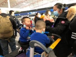 Children adjust their face masks as they and their mother wait in line at check-in counters at Beijing Capital International Airport, in Beijing, China, Jan. 25, 2020.