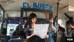  Passengers listen as El Bus TV’s Claudia Lizardo reads a news report. Holding the frame is co-founder Laura Castillo. The service began in May in Caracas, Venezuela, and has spread to other communities. (C. Alcalde/VOA Spanish Service) 