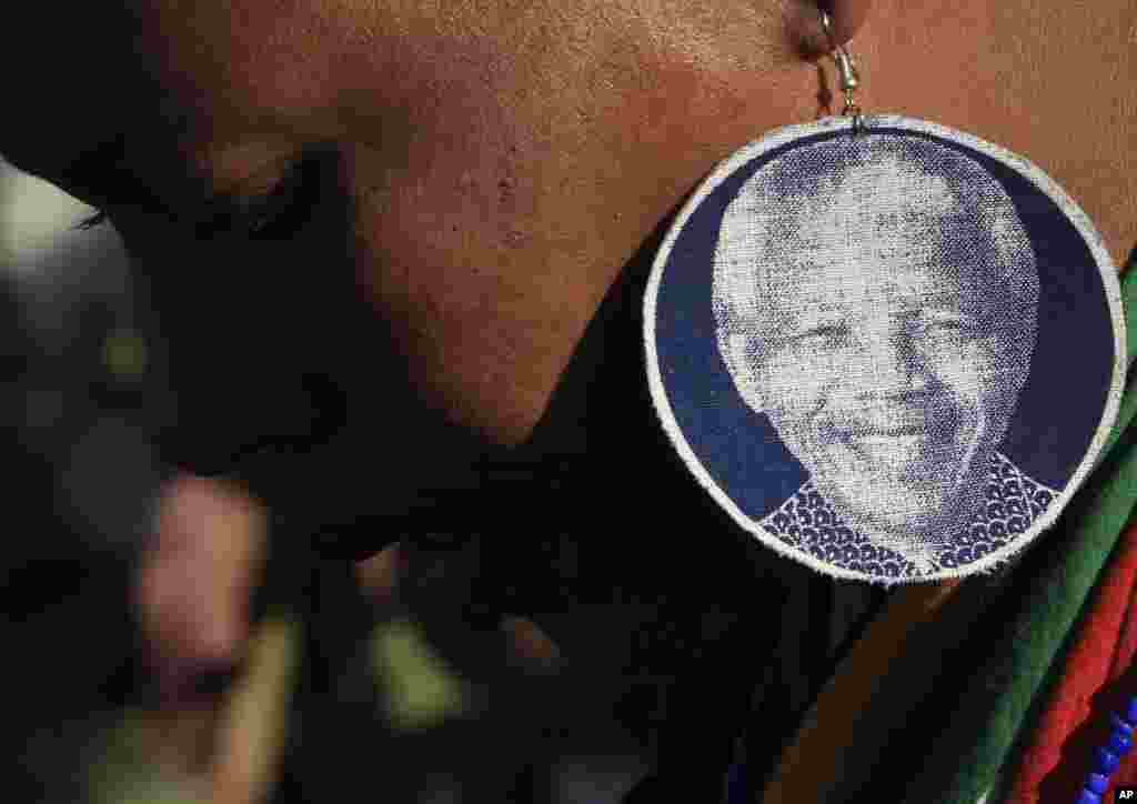 A woman wears earrings bearing the image of former South African President Nelson Mandela, outside the Mediclinic Heart Hospital in Pretoria, June 26, 2013. 