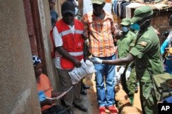 FILE - Member of Uganda's armed forces, and a Red Cross worker distribute foodstuffs to people affected by the lockdown measures aimed at curbing the spread of the new coronavirus, in the Bwaise suburb of Kampala, Uganda, April 4, 2020.