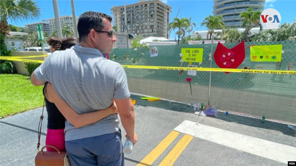 Una pareja observa los mensajes de apoyo en la cerca que limita el paso al &#225;rea del edificio colapsado en Miami Beach.