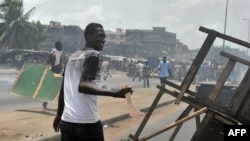 Un homme tient une machette alors que des habitants en colère brûlent des pneus et bloquent la rue pendant des manifestations qui avaient tué au moins six femmes, le 3 mars 2011 à Abobo, un quartier ouvrier de Abidjan. PHOTO AFP / ISSOUF SANOGO (Photo par ISSOUF SANOGO / AFP)