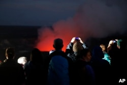 Visitors take pictures as Kilauea's summit crater glows red in Volcanoes National Park, Hawaii, Wednesday, May 9, 2018.