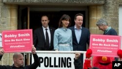 Britain's Prime Minister and Conservative Party leader David Cameron and his wife Samantha leave a voting station in Spelsbury, England, as protesters demonstrate outside after they voted in the general election, May 7, 2015. 