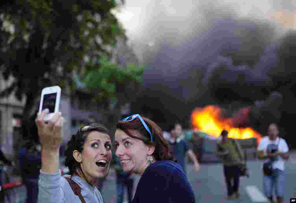 Wisatawan mengambil foto&quot;selfie&quot; ketika para demonstrator membakar sebuah tempat sampah dalam rally May Day di Barcelona, Spanyol, 1 Mei 2014. &nbsp;