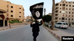 FILE - A militant loyal to Islamic State waves an flag in Raqqa, Syria, June 29, 2014. 