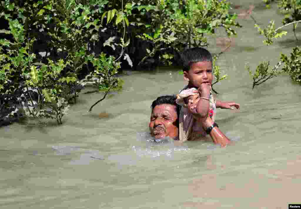 Myanmar&#39;dan Bangladeş&#39;e geçen bir Arakan Müslümanı sınırdaki nehri aşarken çocuğunu sırtında taşıyor.