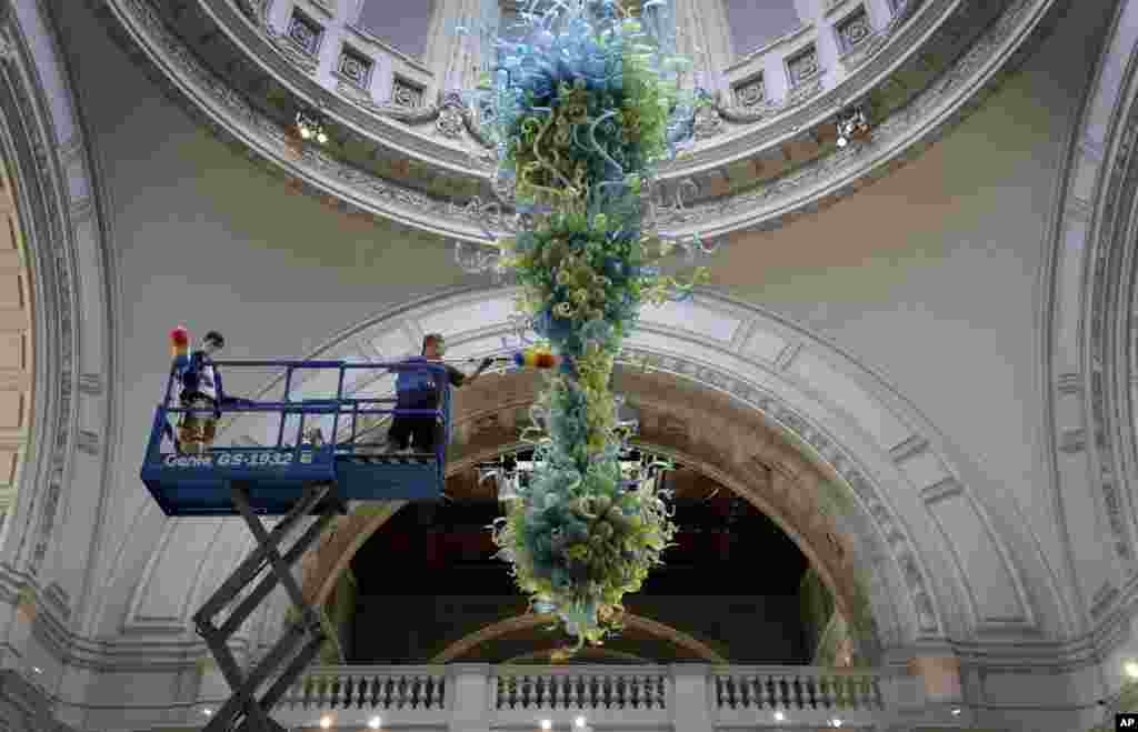 Museum technicians clean one of the V&A's most iconic and largest 27-foot glass chandelier made up of 1,300 exquisite blue and green glass elements, that hangs in the museum's Grand Entrance at the in London, Aug. 4, 2020.
