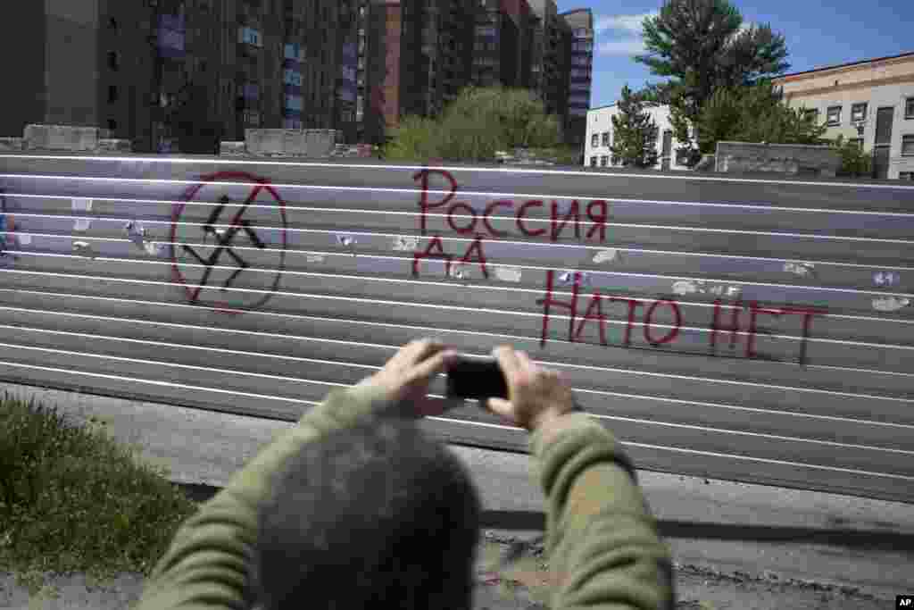 A man takes a picture of graffiti reading, "Russian - yes, NATO - no" with his cell phone in the center of Slovyansk, Ukraine, Tuesday, May 6, 2014. Gunbattles took place at various positions around the city Monday in what has proven the most ambitious government effort to date to quell unrest in the mainly Russian-speaking east. (AP Photo/Alexander Zemlianichenko)