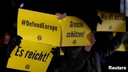 FILE - Demonstrators hold placards with the logo of the far right Identitarian movement during a demonstration against German Chancellor Angela Merkel's migrant policy in Berlin, December 21, 2016.