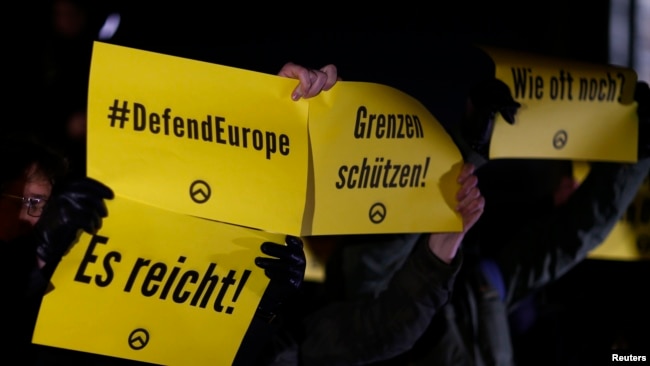 FILE - Demonstrators hold placards with the logo of the far right Identitarian movement during a demonstration against German Chancellor Angela Merkel's migrant policy in Berlin, December 21, 2016.