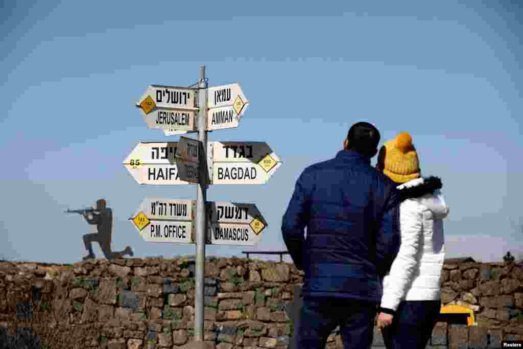 A couple looks at signs pointing out distances to different cities, on Mount Bental, an observation post in the Israeli-occupied Golan Heights that overlooks the Syrian side of the Quneitra crossing, Israel.