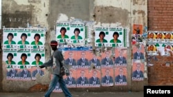 Des affiches de campagne placardées sur un bâtiment vétuste à quelques mètres d’un bureau de vote où se rend cet électeur malgache - Madagascar, 25 octobre 2013.