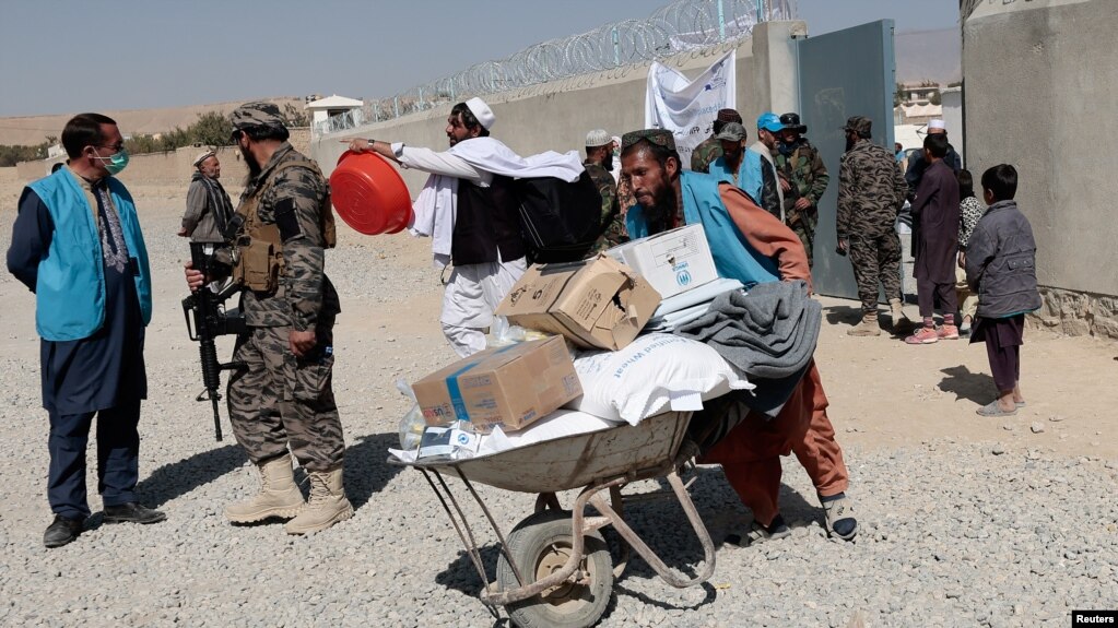 FILE - A local aid worker from pushes a wheelbarrow loaded with aid supplies outside a distribution center as a Taliban fighter secures the area, on the outskirts of Kabul, Afghanistan, Oct. 28, 2021.