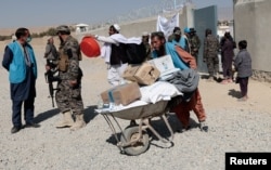A worker from UNHCR pushes a wheelbarrow loaded with aid supplies for a displaced Afghan family outside the distribution center as a Taliban fighter secures the area on the outskirts of Kabul, Afghanistan, Oct. 28, 2021.