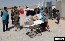 A UNHCR worker shoots a wheelbarrow loaded with aids for a displaced Afghan family outside the distribution center when a Taliban fighter secures the area on the outskirts of Kabul, Afghanistan, October 28, 2021.