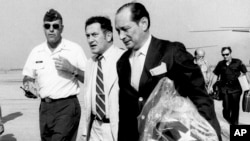In this April 12, 1975, file photo, U.S. Ambassador to Cambodia John Gunther Dean carries the American flag from the U.S. Embassy in Cambodia as he arrives at Utapao Air Force Base in Thailand following the evacuation from Phnom Penh by helicopter and aircraft carrier.