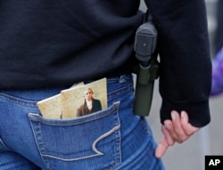 FILE - a woman wears a gun next to two copies of the U.S. Constitution during a gun rights rally at the Capitol in Olympia, Wash.