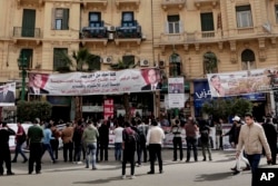 FILE - People hold banners showing support for Egyptian presidential candidates on a street in downtown Cairo, March 4, 2018.
