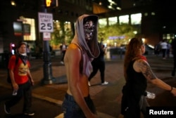 A masked demonstrator walks the streets of downtown past midnight as people protest the police shooting of Keith Scott in Charlotte, North Carolina, U.S., September 23, 2016.