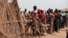 FILES - Ali Abdula, 16, guides his donkey carrying his two younger siblings, both suffering from malnutrition, past people lining up to register for aid at a camp for internally displaced persons (IDP) in Agari, South Kordofan, June 17, 2024. 