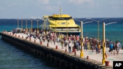 FILE - Tourists and passengers disembark from a ferry onto the wharf on Playa del Carmen, Mexico, March 2, 2018. The U.S. Embassy in Mexico has narrowed its travel warning for the city amid what it calls an unspecified security threat. 