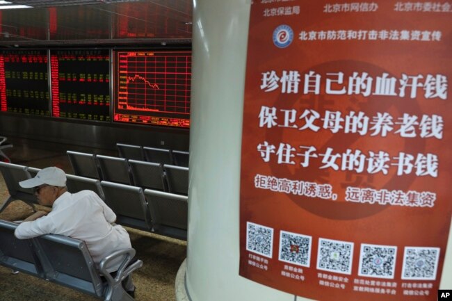 北京一名投资者坐在一个股票交易所内树立的一张海报旁。海报上写道：“珍惜自己的血汗钱，保卫父母的养老钱，守住子女的读书钱“。(2019年6月12日)
