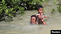 Seorang pengungsi Rohingya menggendong anaknya sambil berenang menyeberangi sungai di perbatasan Rakhine, Myanmar dan Palang Khali, Bangladesh (foto: dok).