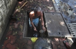 FILE - A laborer cleans a manhole on a sidewalk in Mumbai, India, June 10, 2020.